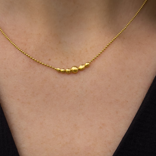 Gold necklace with small gold orbs on a person's neck