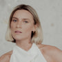 Woman with short blonde hair wearing a white top and tapered gold hoop earrings against a neutral background