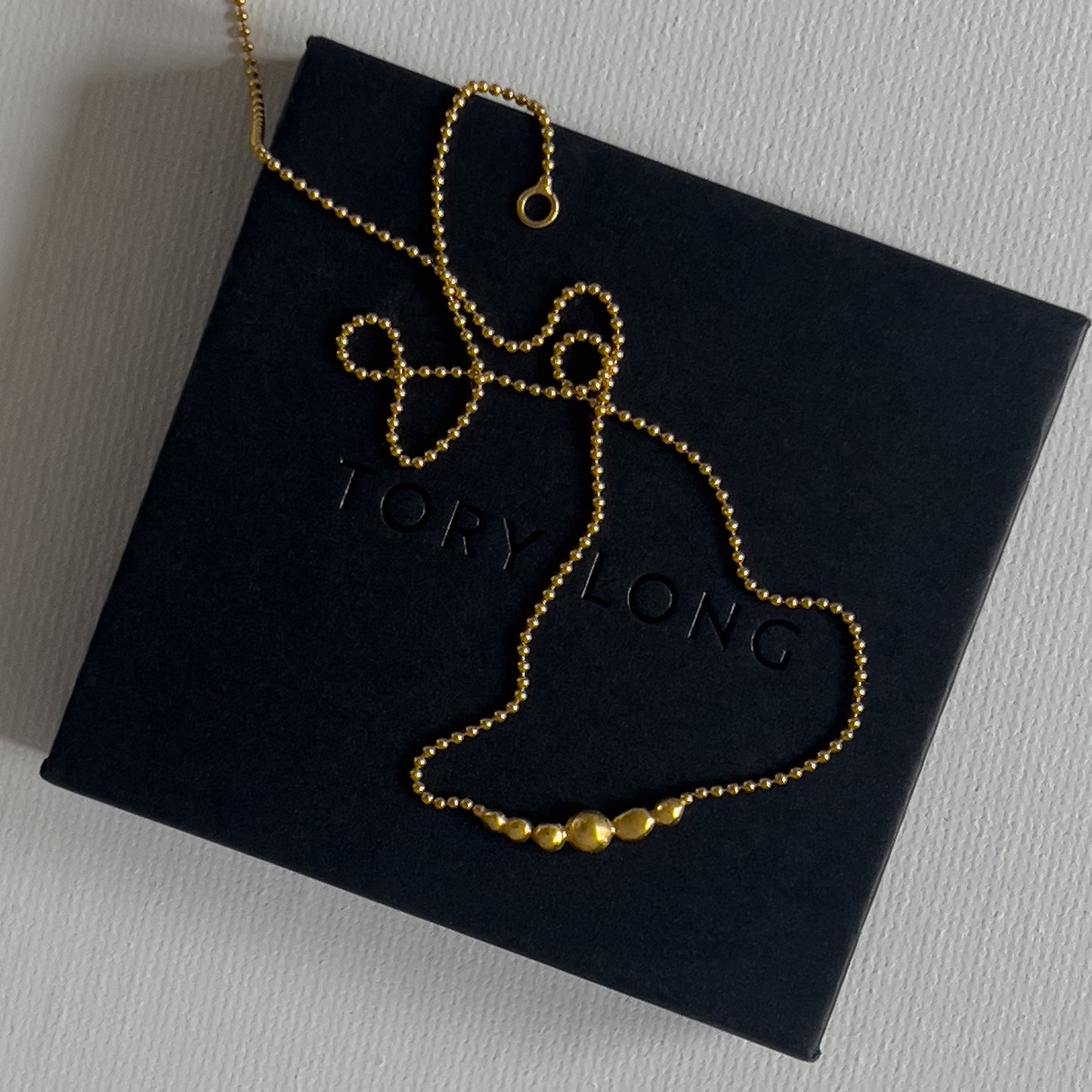 Gold necklace on a black box with 'Tory Long' branding