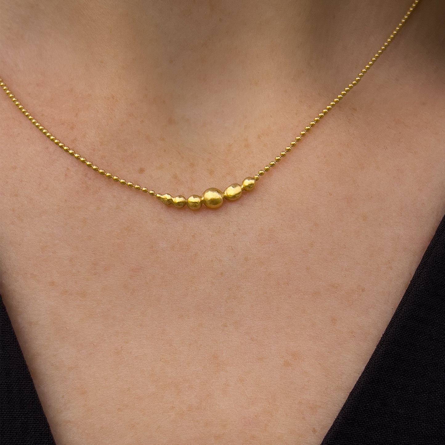 Gold necklace with small gold orbs on a person's neck