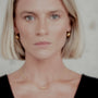 Woman wearing a gold orb necklace and gold orb earrings against a neutral background