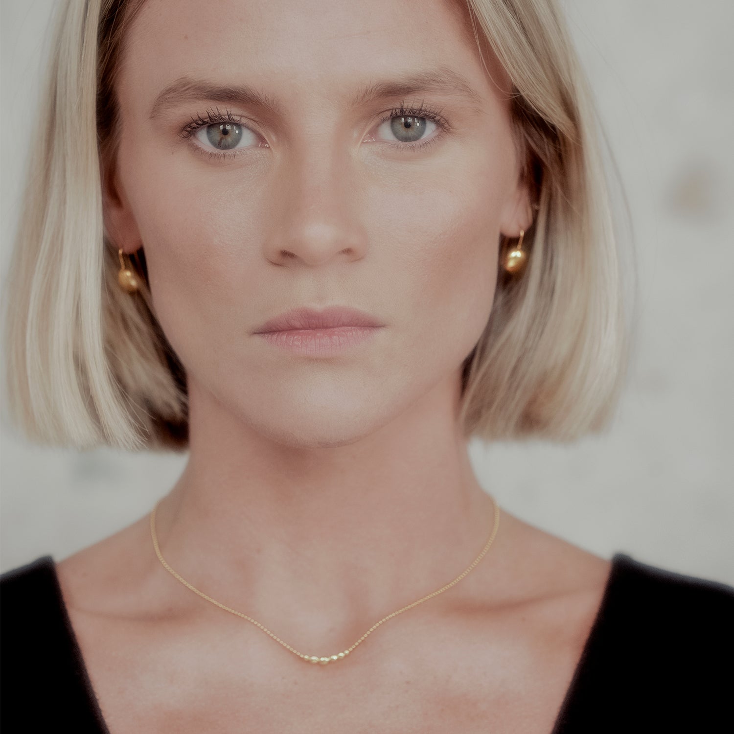 Woman wearing a gold orb necklace and gold orb earrings against a neutral background