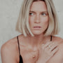 Woman with blonde hair wearing a black top and two layered gold orb necklaces against a neutral background