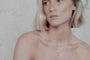 Woman with short blonde hair wearing two gold orb necklaces layered against a neutral background