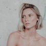 Woman with short blonde hair wearing two gold orb necklaces layered against a neutral background