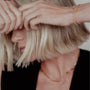 Close-up of a person with short blonde hair and gold paperclip necklace, gold love knot rings and gold birthstone bracelets. 
