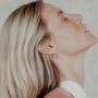 Woman with blonde hair wearing a gold tapered hoop earring against a neutral background