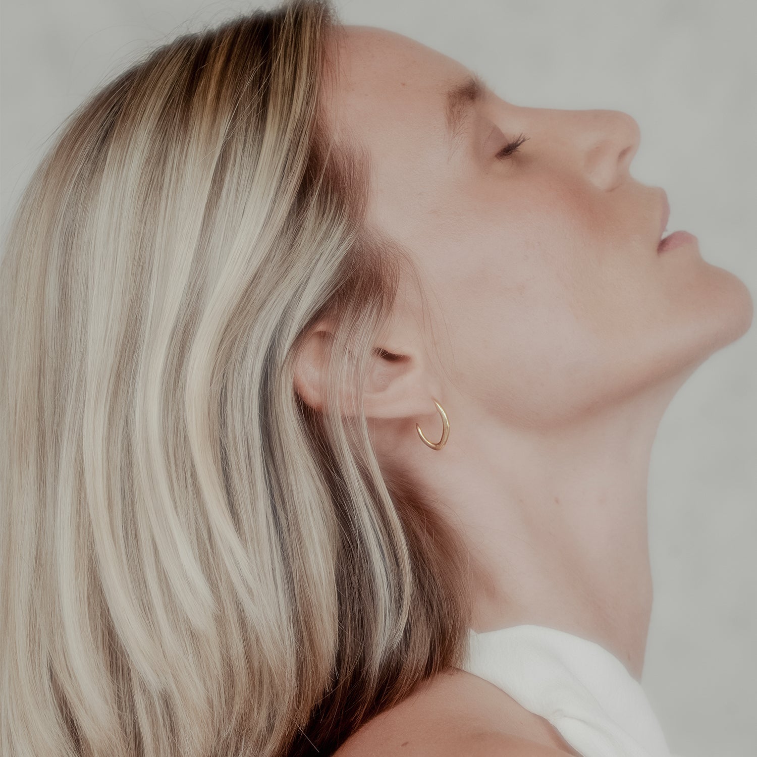 Woman with blonde hair wearing a gold tapered hoop earring against a neutral background