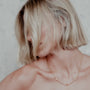 Person with short blonde hair wearing a gold ball chain necklace with 3 spikes against a neutral background