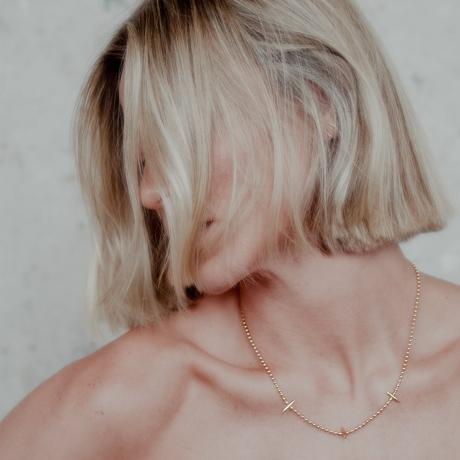Person with short blonde hair wearing a gold ball chain necklace with 3 spikes against a neutral background