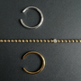 Gold and silver rings and a gold ball chain bracelet with a white lab diamond on a dark gray background