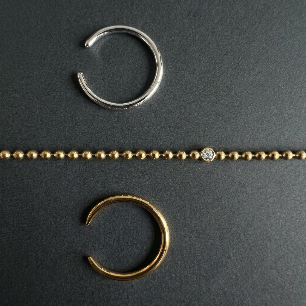 Gold and silver rings and a gold ball chain bracelet with a white lab diamond on a dark gray background
