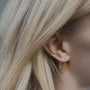 Close-up of an ear wearing gold and silver hook hoop earrings with blonde hair.