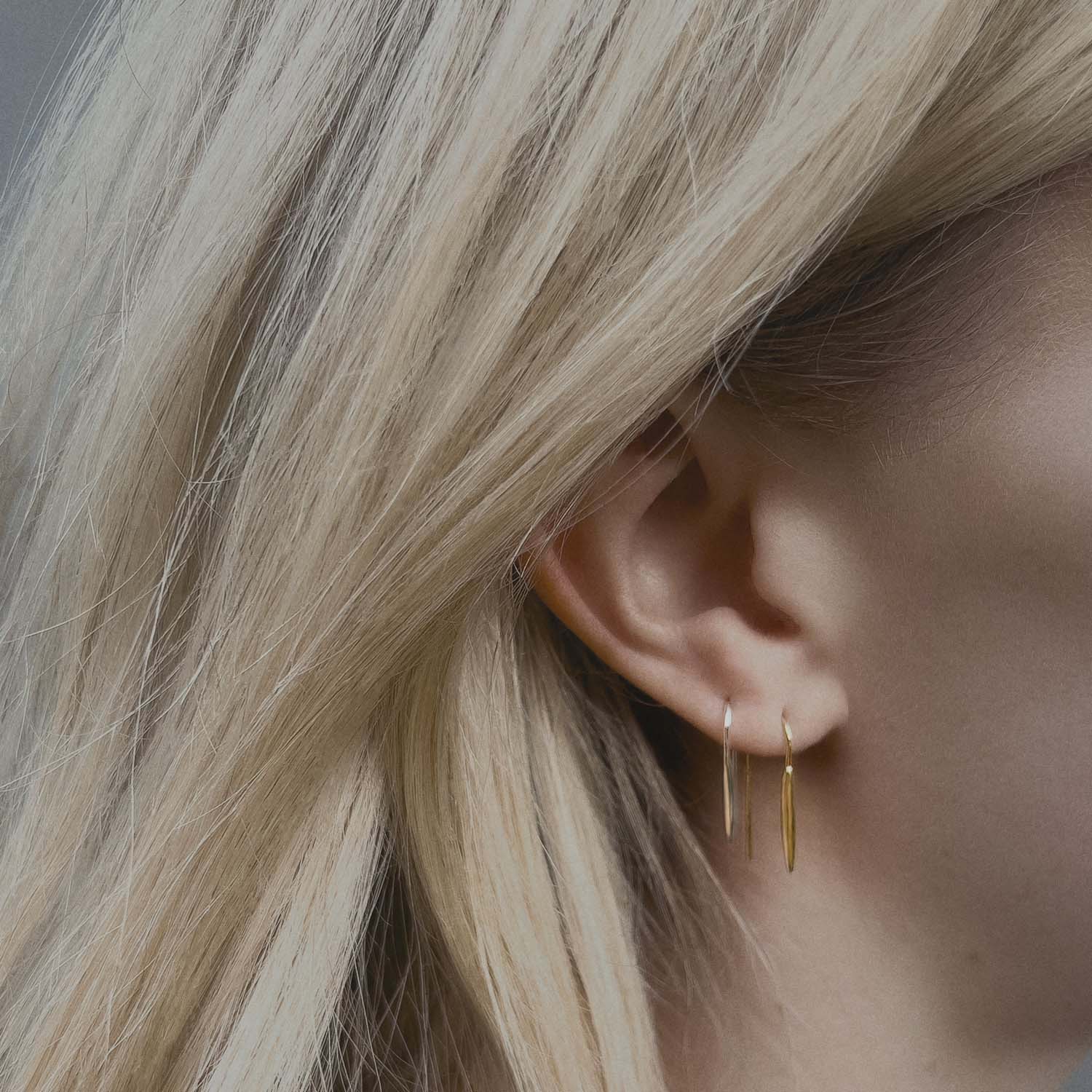 Close-up of an ear wearing gold and silver hook hoop earrings with blonde hair.
