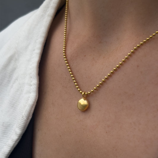 Gold necklace with a pendant on a person wearing a white shirt.