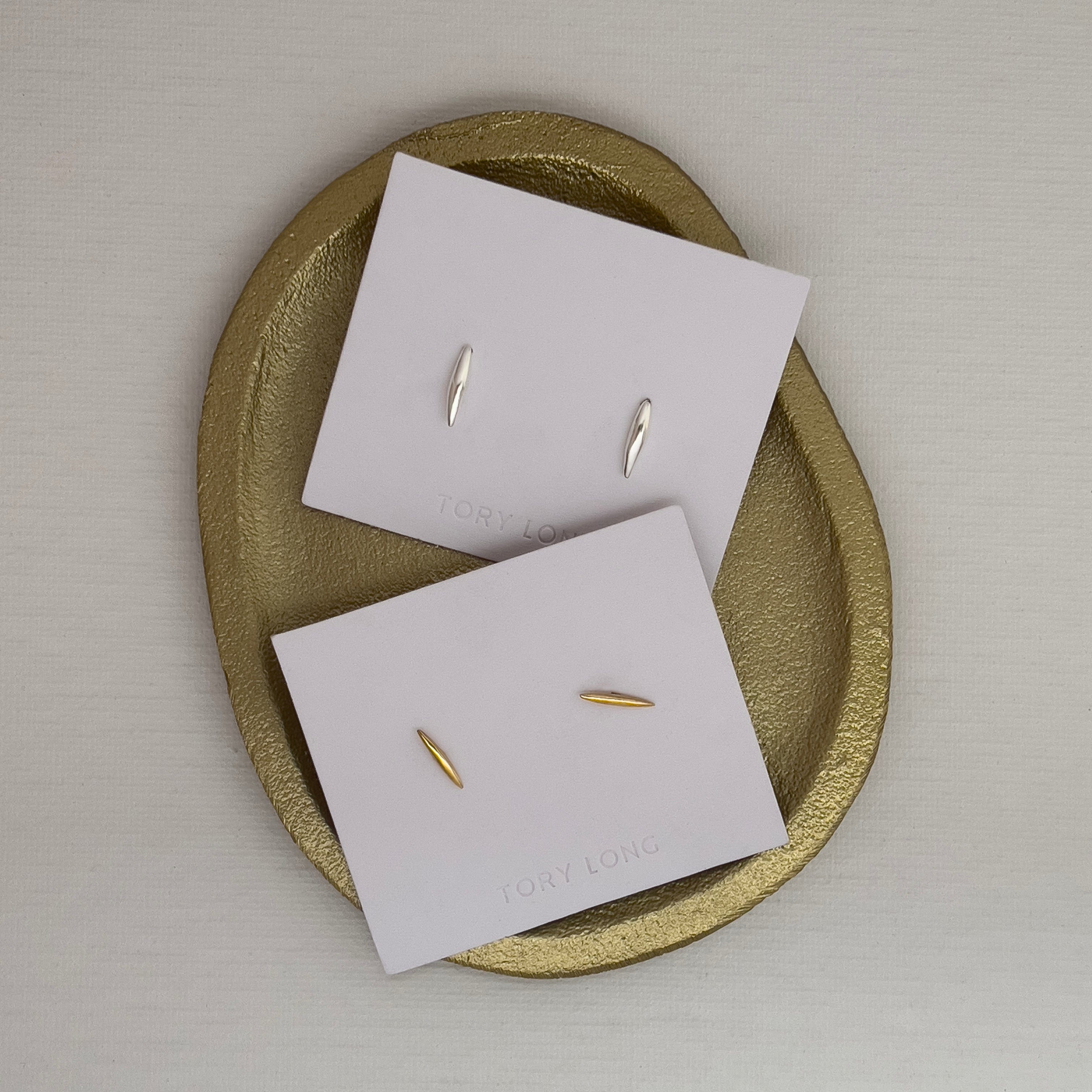 Gold earrings on white cards with a gold dish on a light gray background