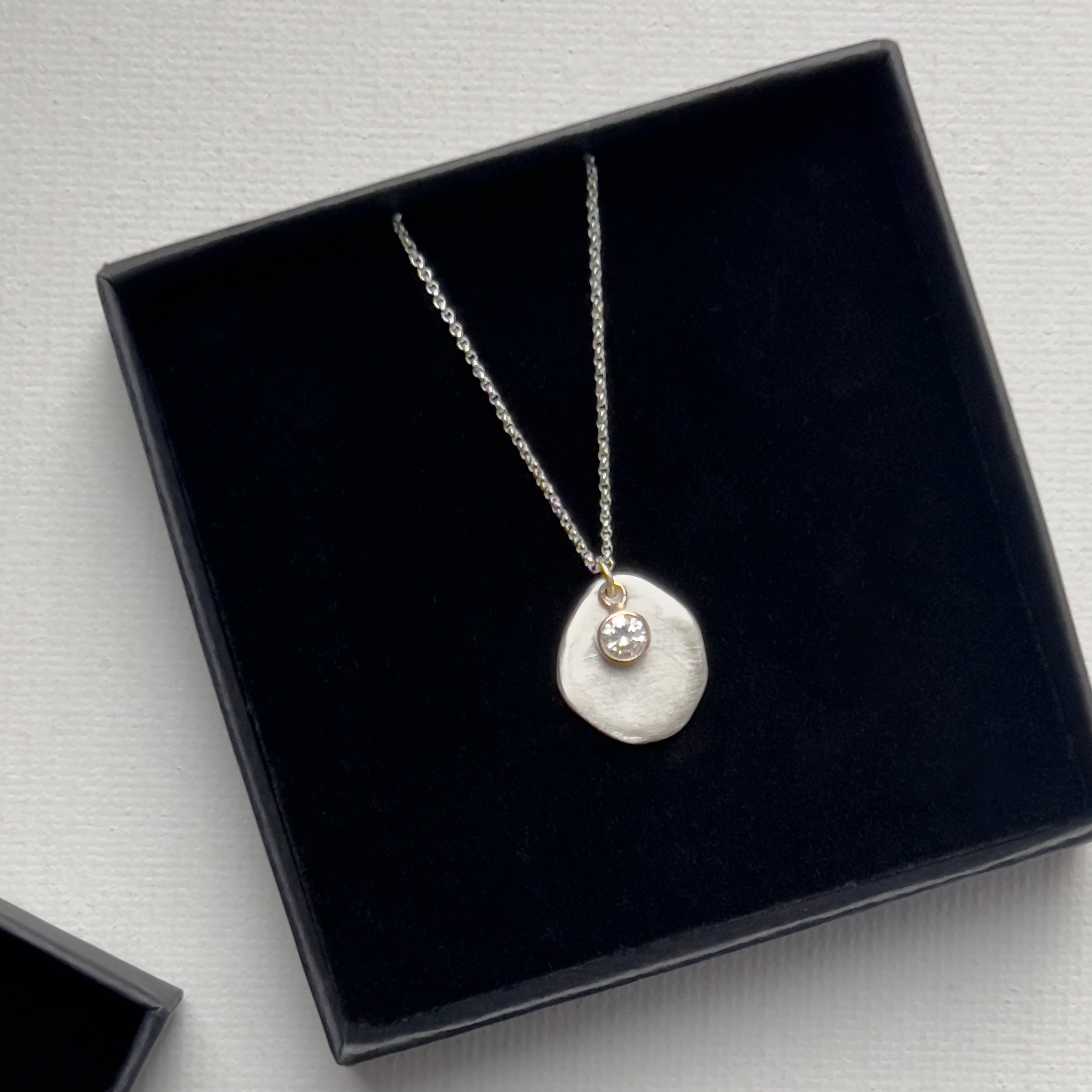 Sterling silver necklace with a silver and diamond pendant in a black jewelry box on a light gray background