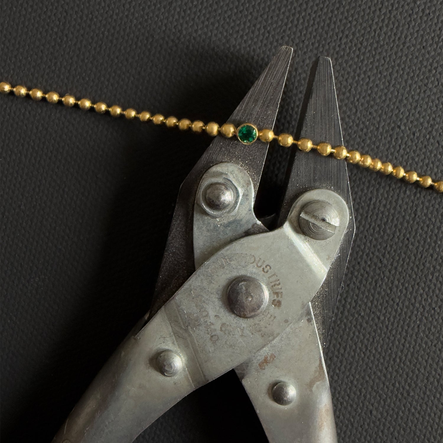 Pair of pliers cutting a gold chain with a green emerald bracelet on a dark background