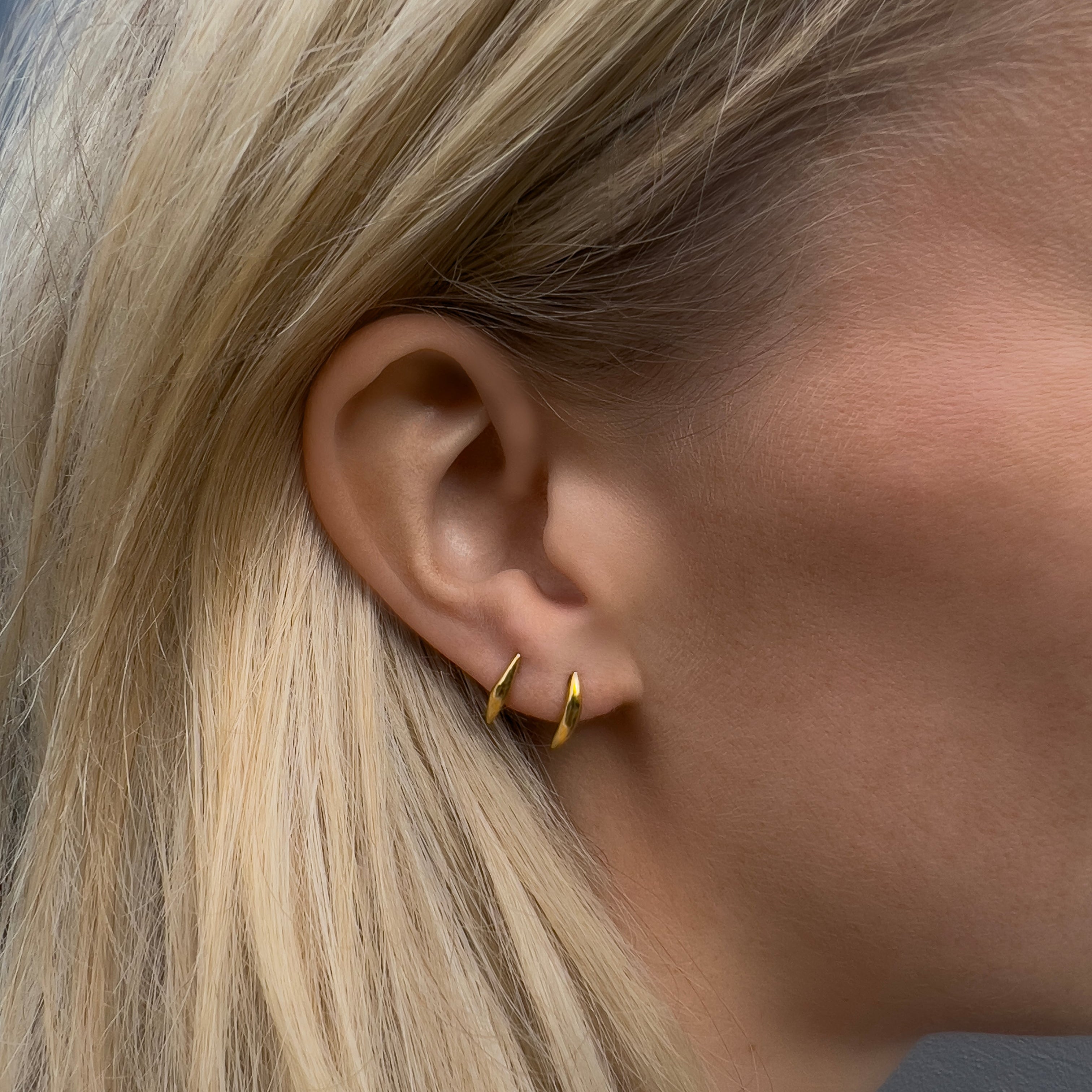 Close-up of an ear wearing a gold earring with blonde hair and blurred background