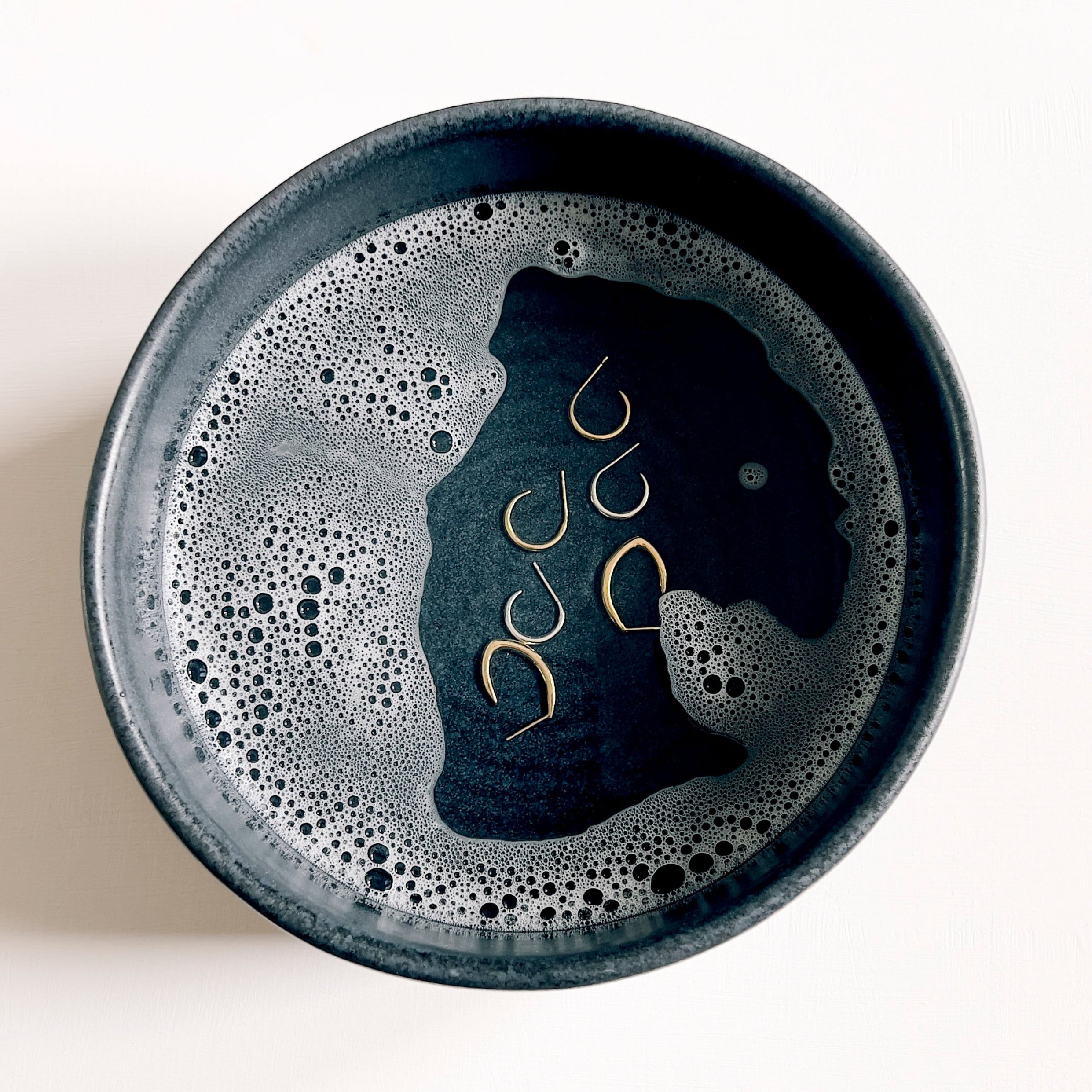 Gold and silver earrings placed in a bowl of warm soapy water for cleaning