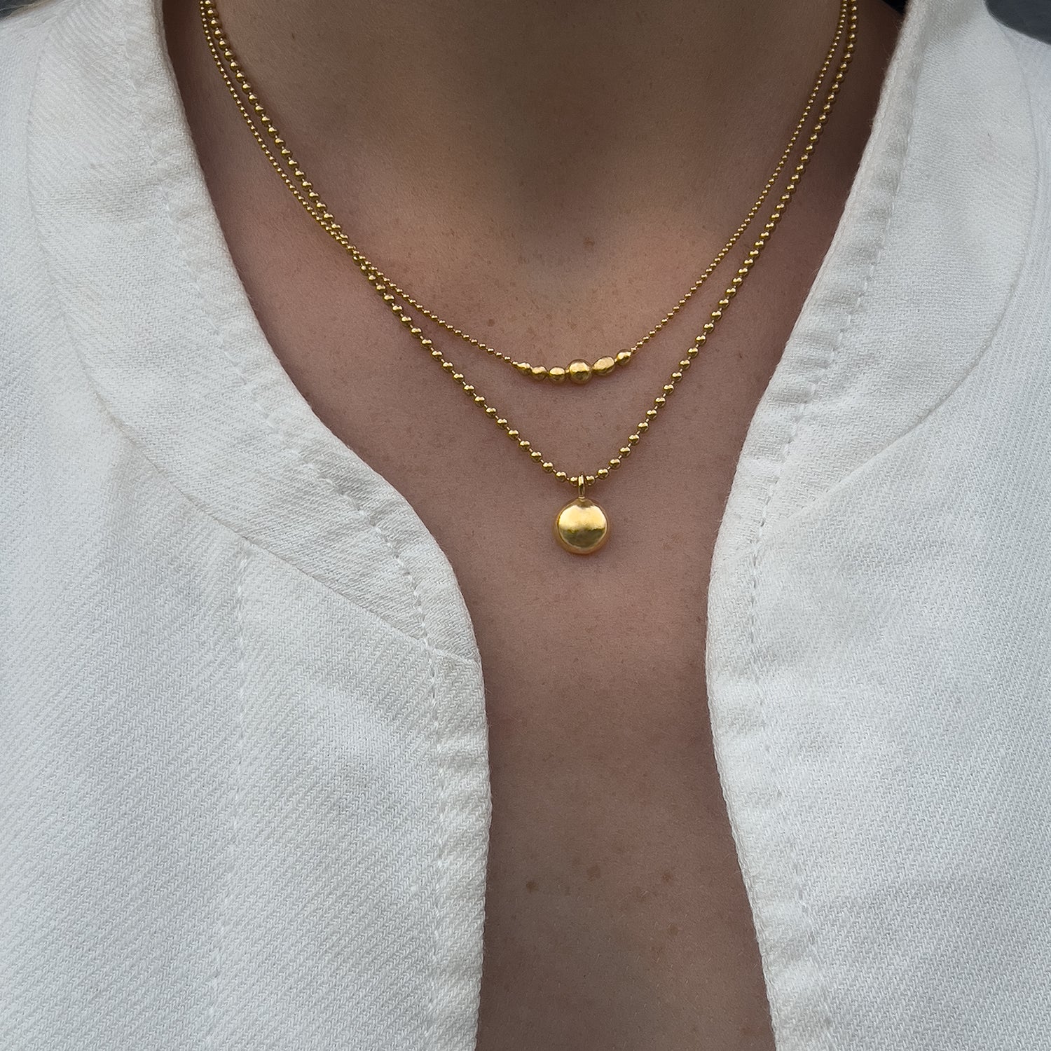 Layered Gold necklaces on a person wearing a white top