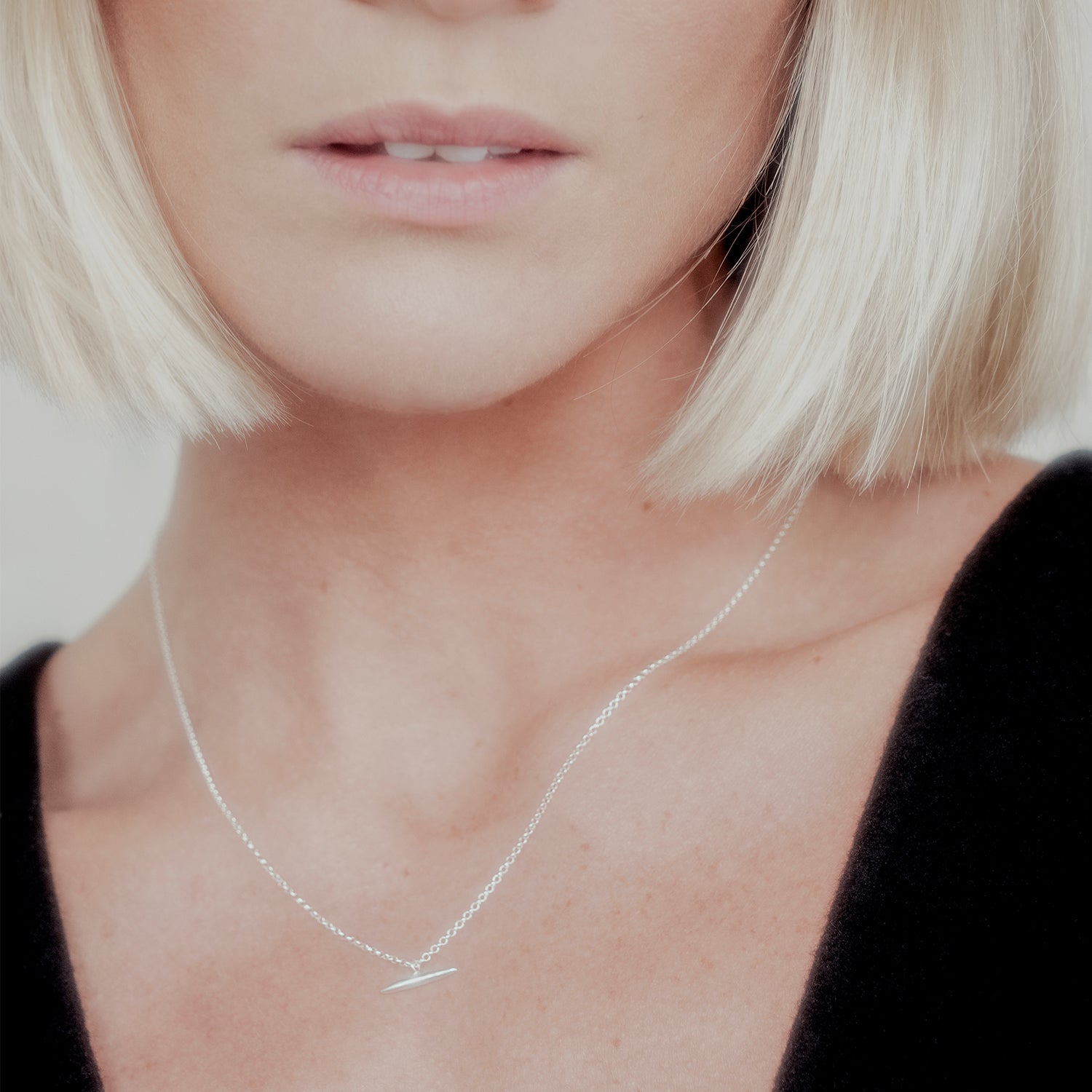 Close-up of a person wearing a delicate silver chain necklace with a minimalistic tapered bar pendant.