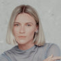Woman with blonde hair wearing silver hoop earrings against a plain background