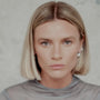 Woman with blonde hair and silver orb earrings wearing a gray top against a neutral background
