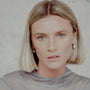 Woman with blonde hair and silver orb earrings wearing a gray sweater against a neutral background