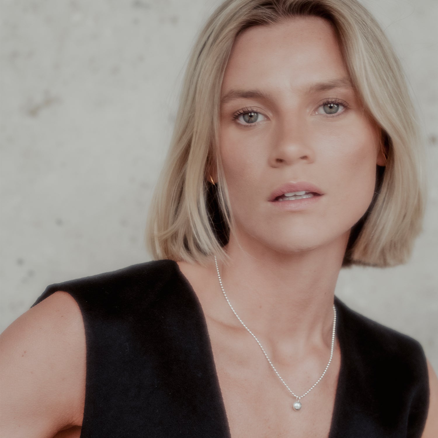 Woman wearing a black sleeveless top and a silver orb necklace against a neutral background