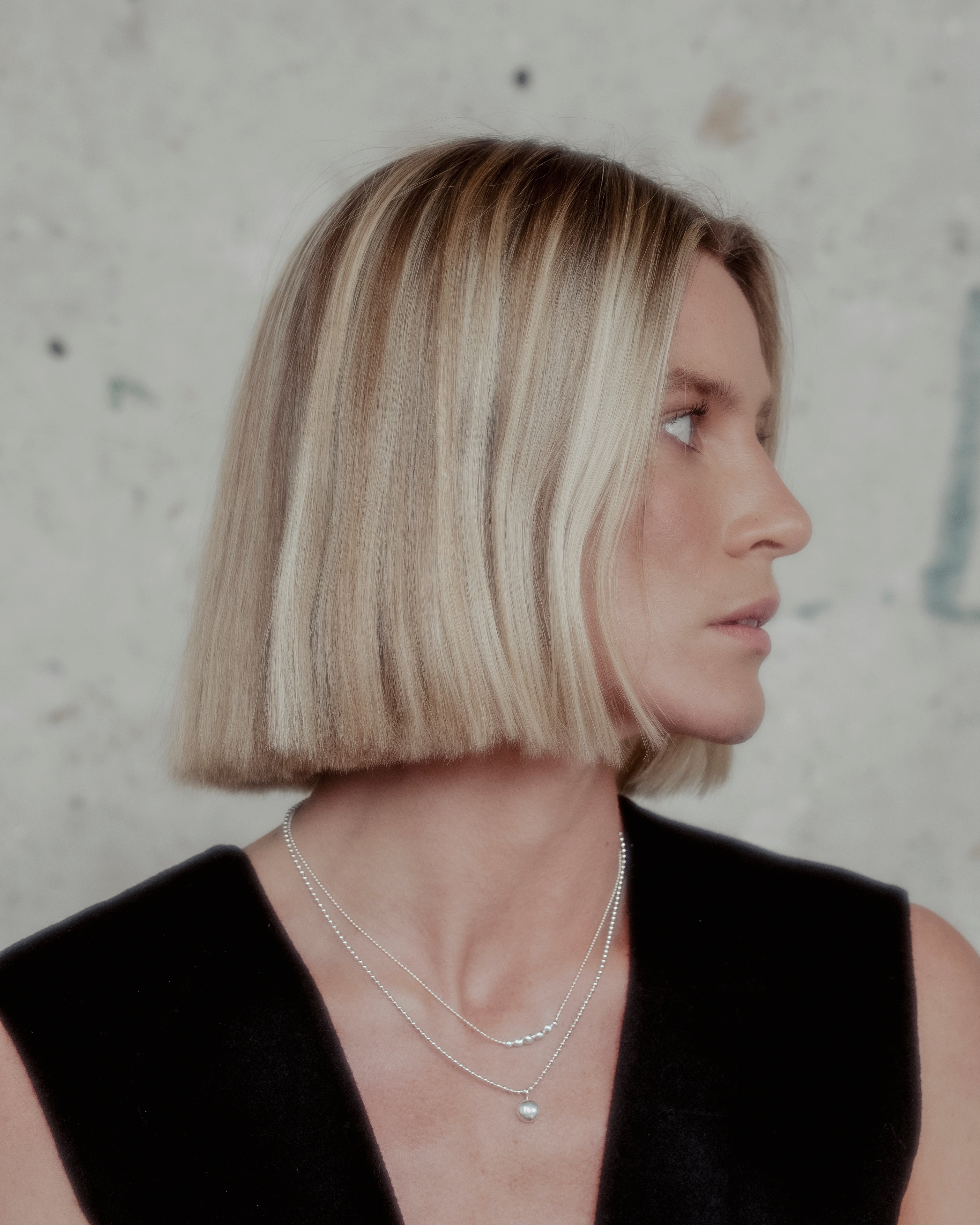 Woman with a bob haircut wearing a black sleeveless top and layered ball chain sterling silver orb necklaces against a neutral background