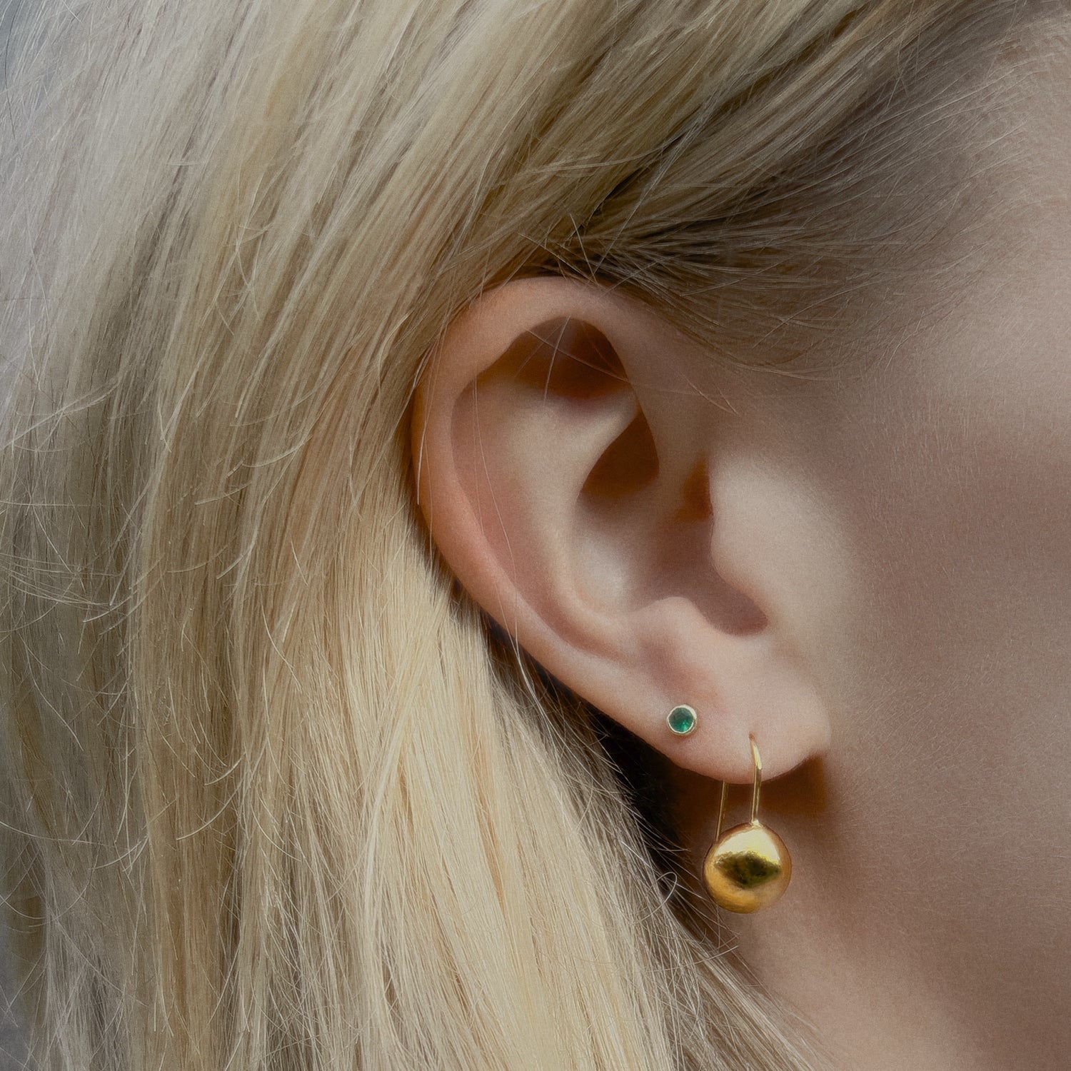 Close-up of an ear wearing a gold orb drop earring with a green agate gemstone stud. 