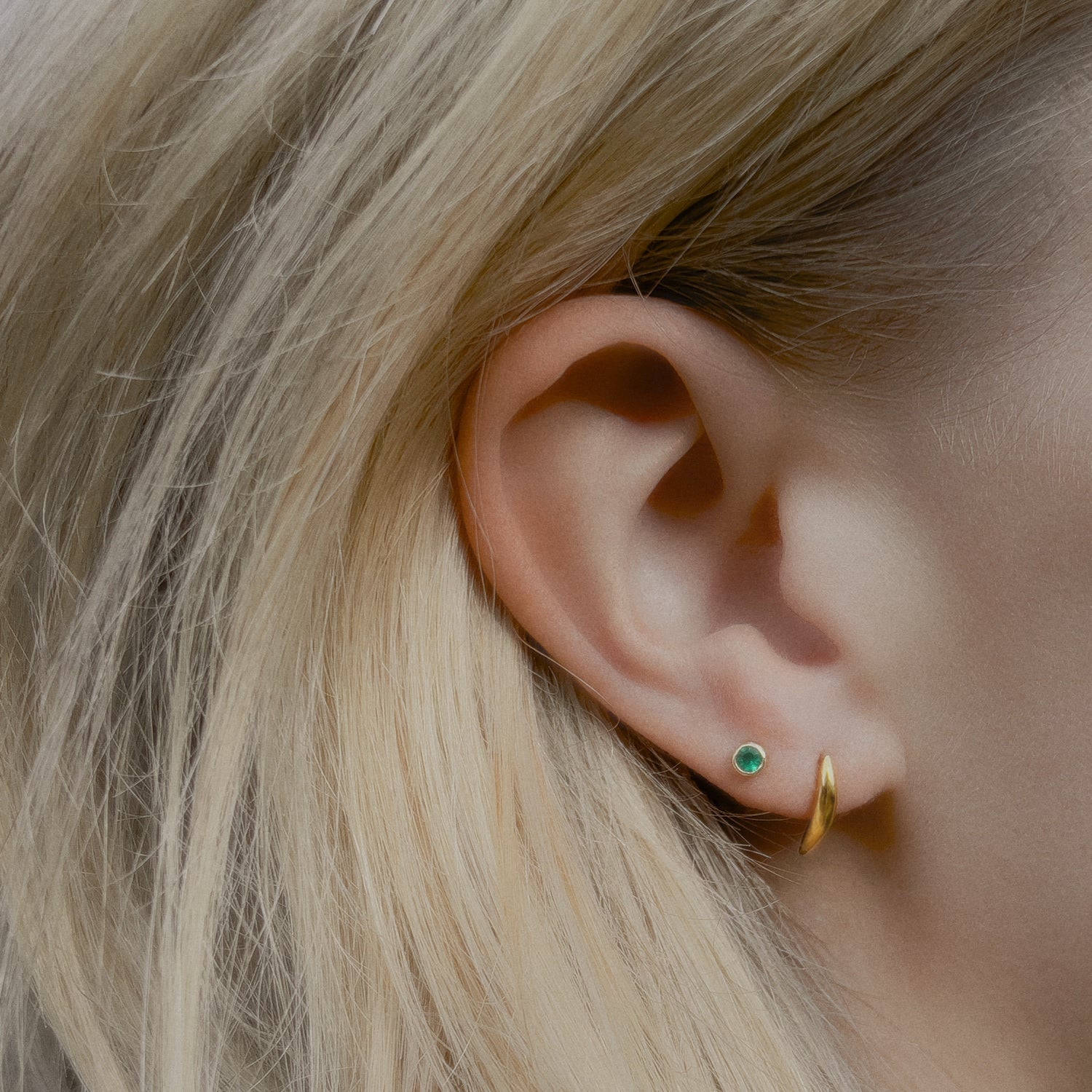 Close-up of an ear wearing a gold curve stud earring with a green agate gemstone stud. 
