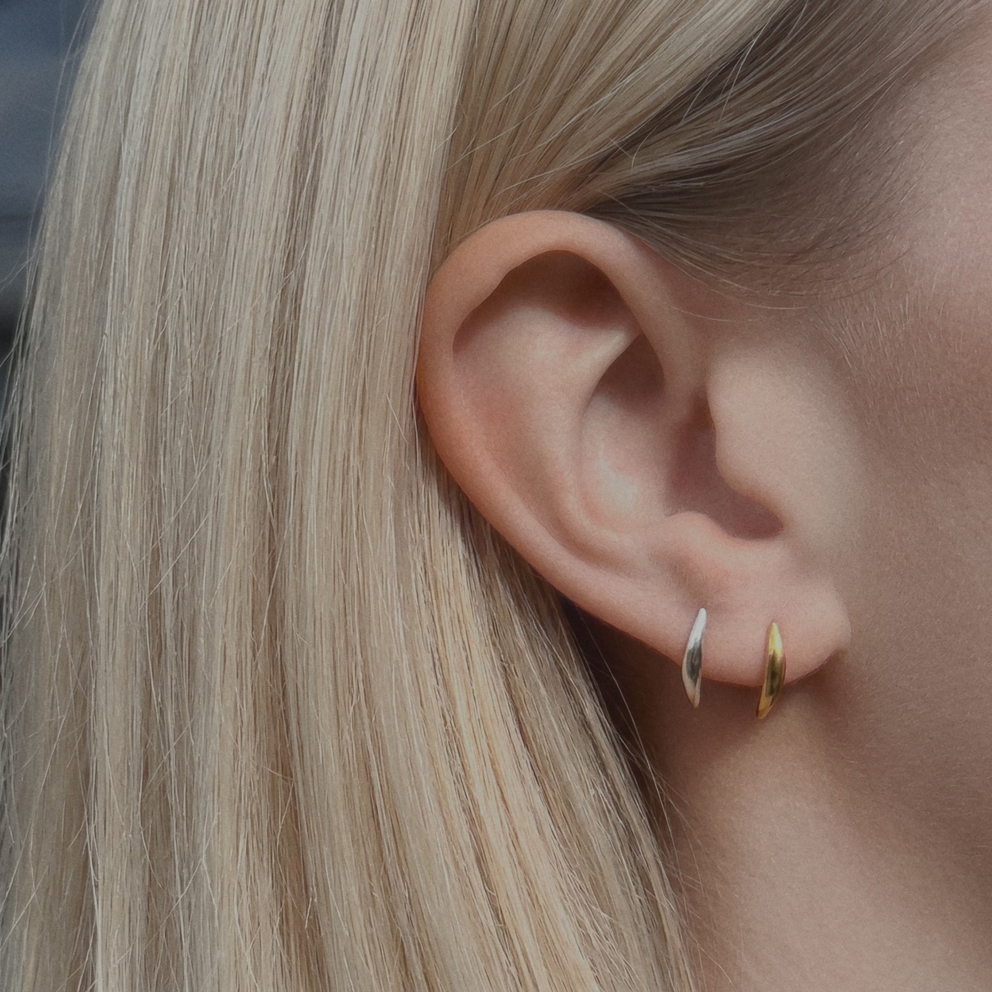 blonde woman wearing silver and gold curved stud earrings